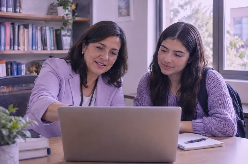 Asesora de empleabilidad revisa con un estudiante su avance en la computadora.